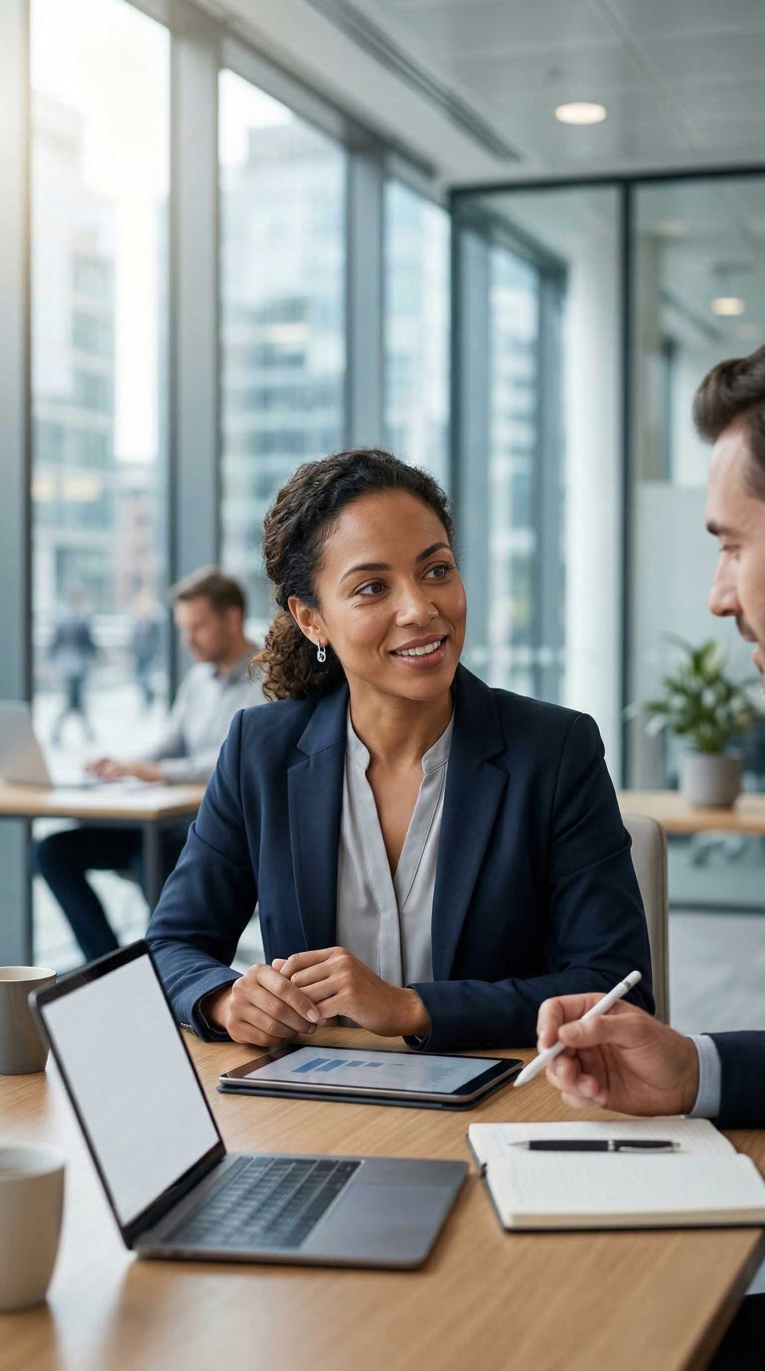 A smiling businesswoman in a blazer discusses B2B growth strategies with a colleague in a modern office.