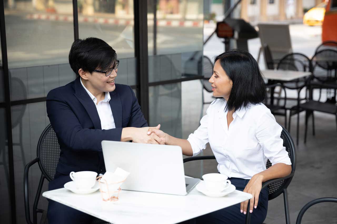 Professional B2B handshake at a cafe table with a laptop.