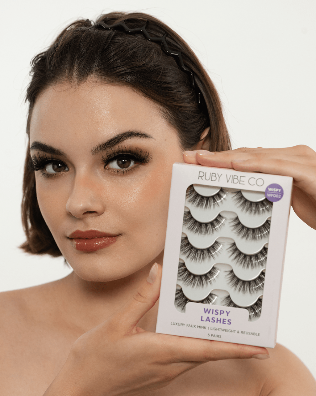 A model wearing dramatic, wispy eyelashes holds up a 5-pack of Ruby Vibe Co