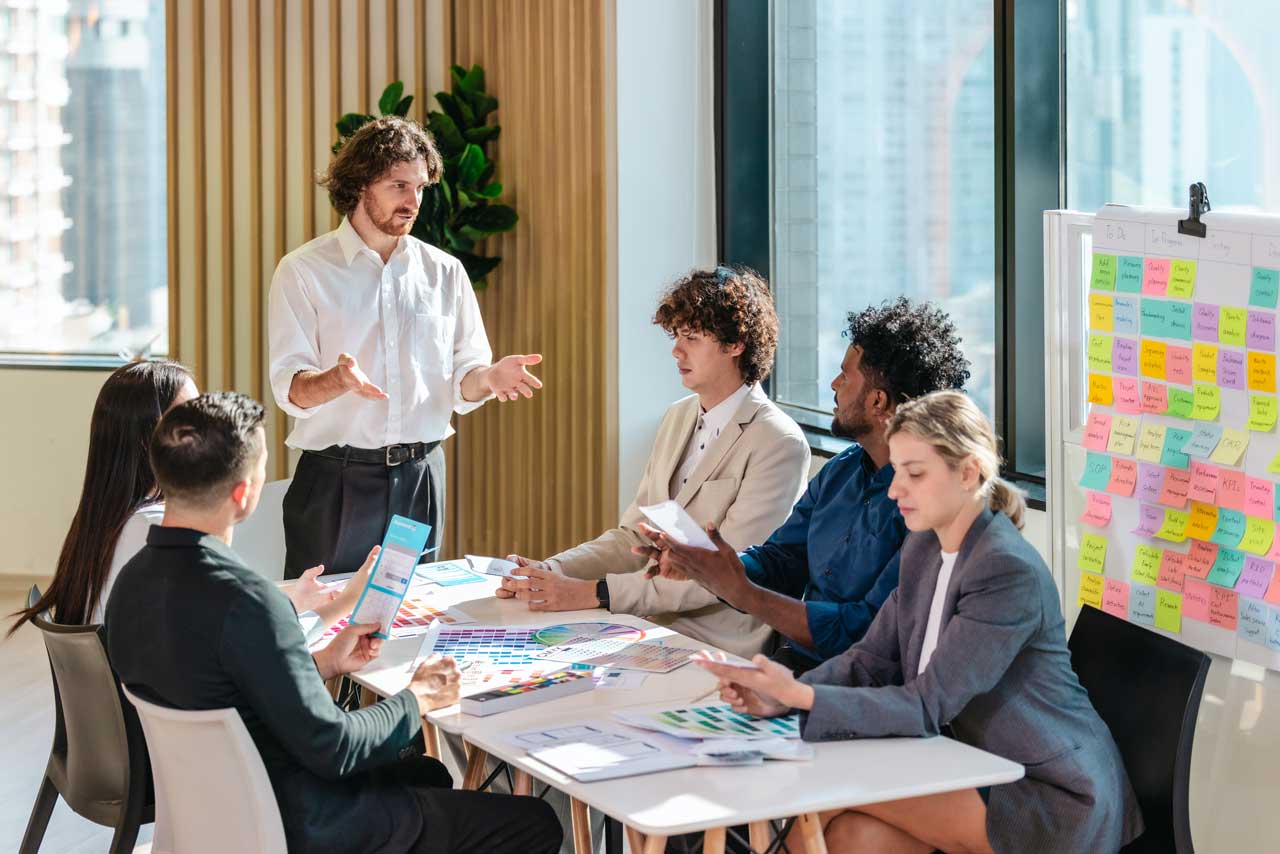 Professional team discussing B2B sales strategies around a table with a sticky-note planning board in a modern office.