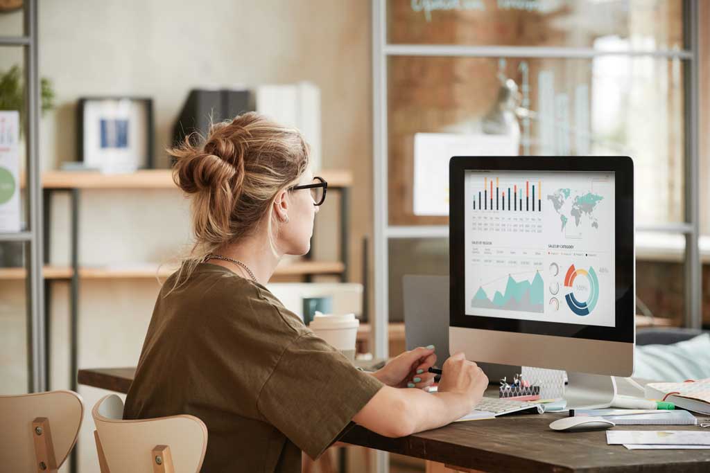 Professional analyst monitoring data dashboard with global charts on an iMac computer at a Pixel Commercial Studio desk