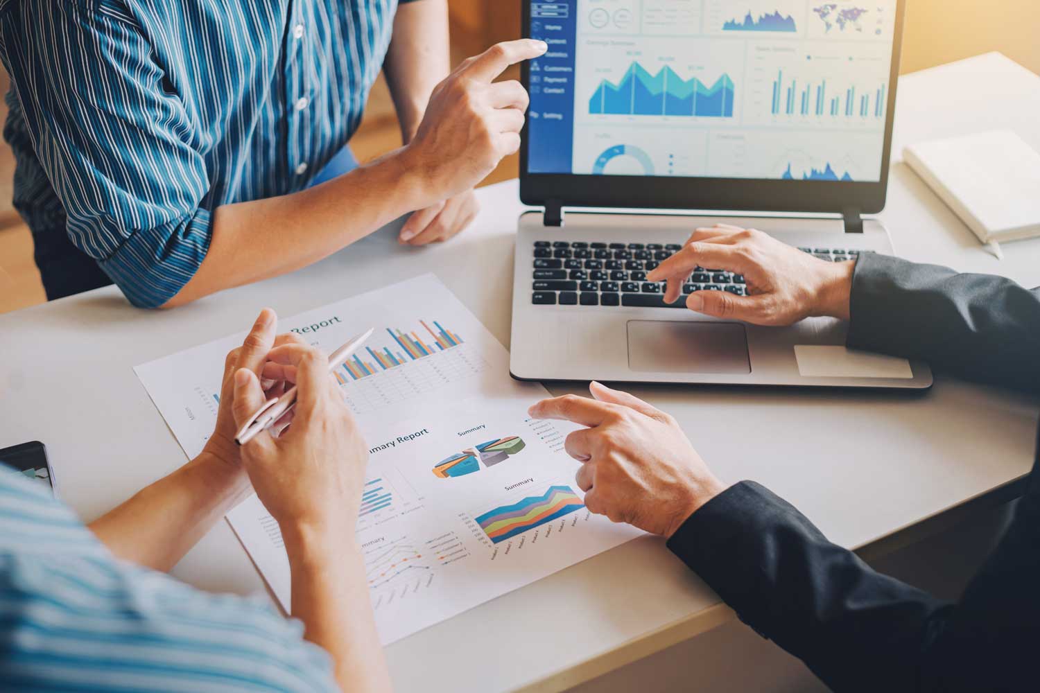 Close-up of professionals reviewing marketing data charts on a laptop and printed reports for business growth.
